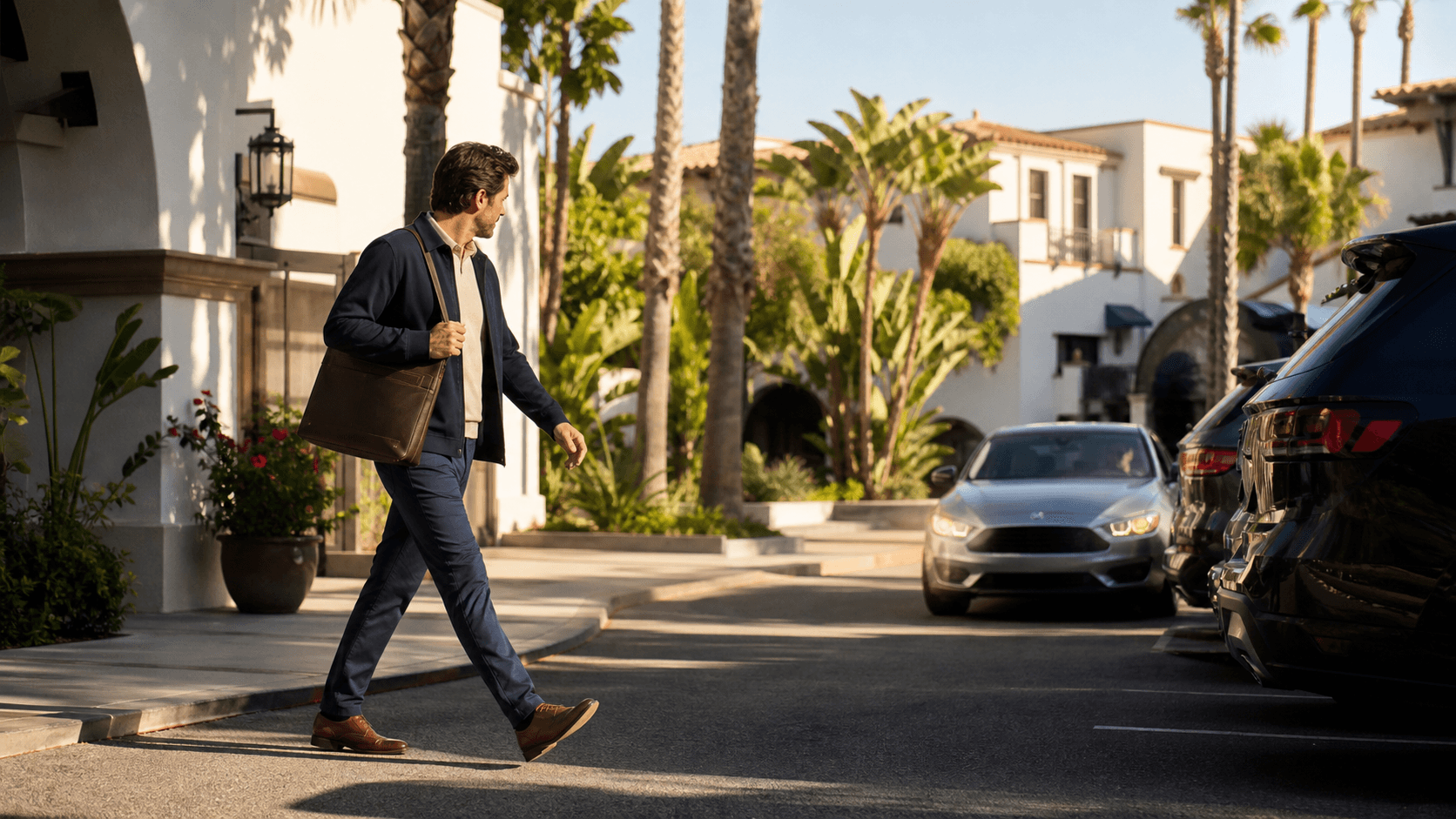 Sunlit Santa Barbara crosswalk with pedestrians, palm trees, parked cars, and mountains in the distance.